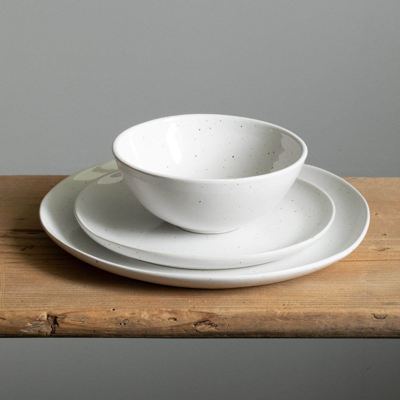 Un bol de céréales est posé sur une petite assiette de petit-déjeuner, sous laquelle se trouve une grande assiette de plat principal organique en blanc brillant avec de fines éclaboussures dorées.