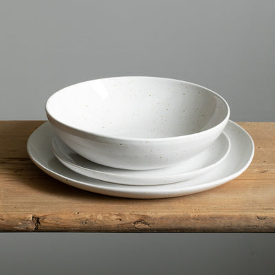 Grande et petite assiette superposées et, par-dessus, une assiette de pâtes de couleur blanche avec des éclaboussures de peinture dorée