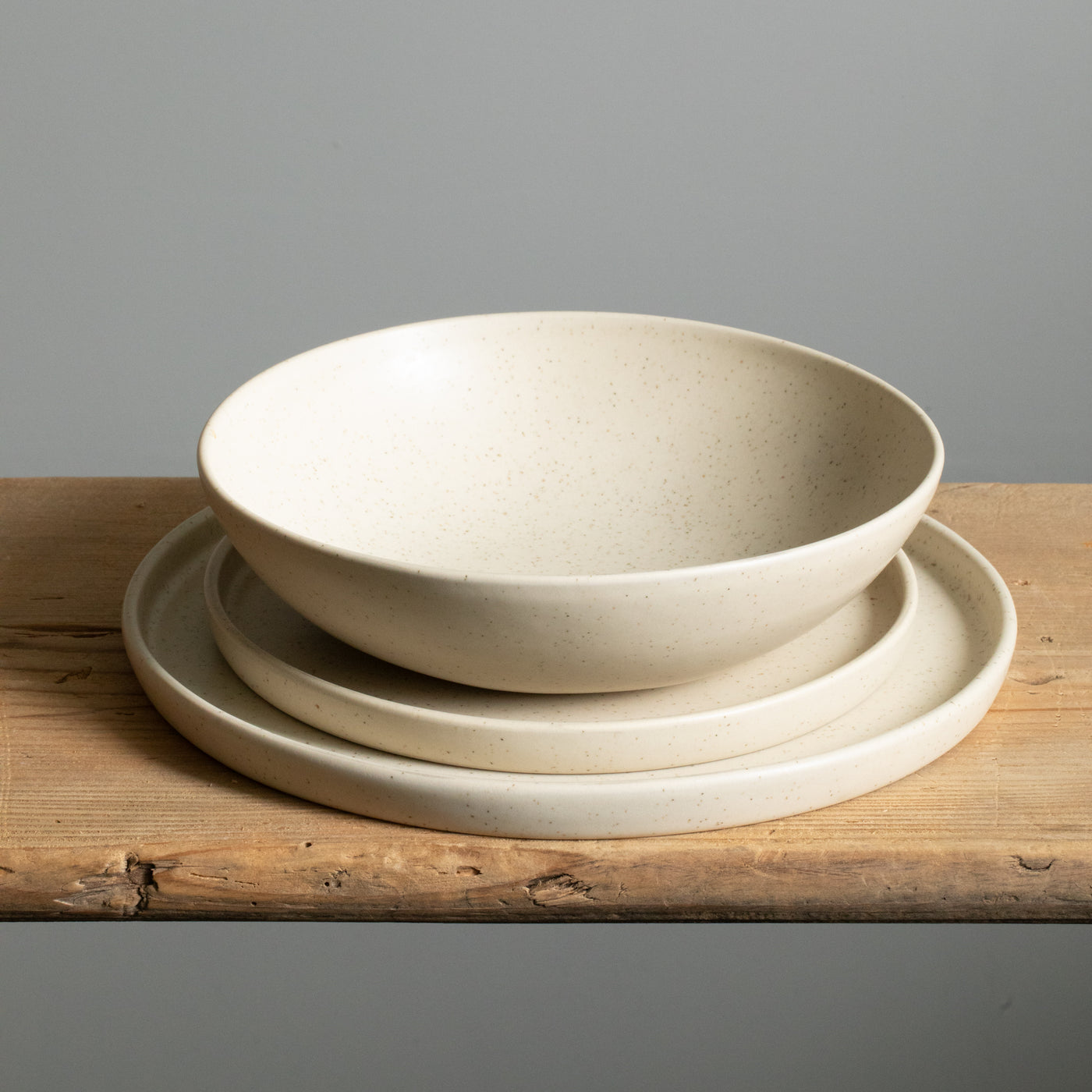Une grande assiette, une petite assiette avec un rebord et une assiette creuse pour les pâtes, le tout empilé dans un glaçage beige.