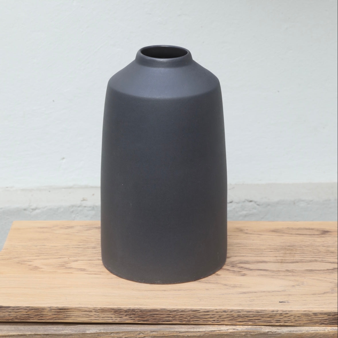 Le vase noir mat, avec une petite ouverture en haut et une large partie inférieure, est posé sur une planche en bois.