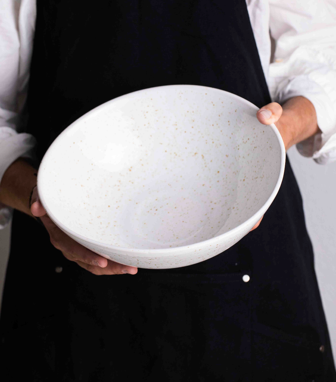Grand saladier blanc tenu par deux mains.